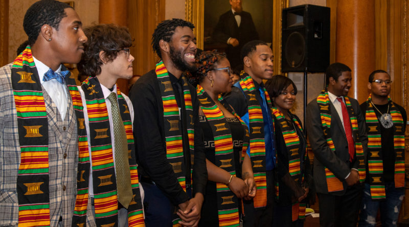 Group of people in a row at a graduation. They are wearing Kente cloth graduation sashes.