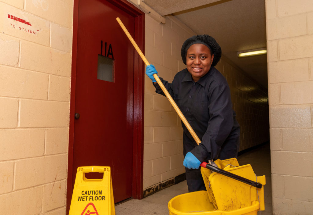 Woman holding a mop and a bucket inside a NYCHA building.