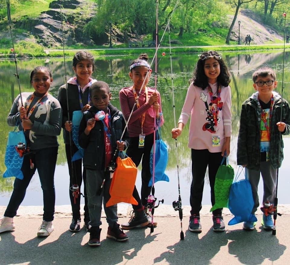 children holding fishing poles standing in front of a lake