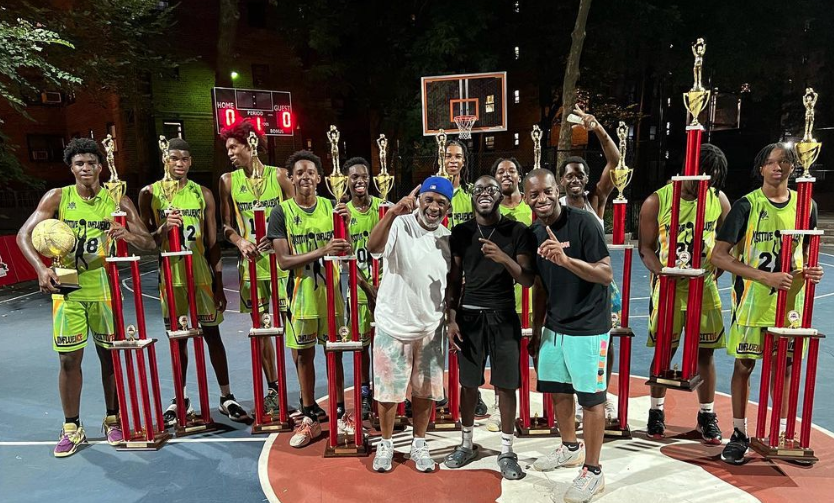 group of people standing on basketball court with large trophies