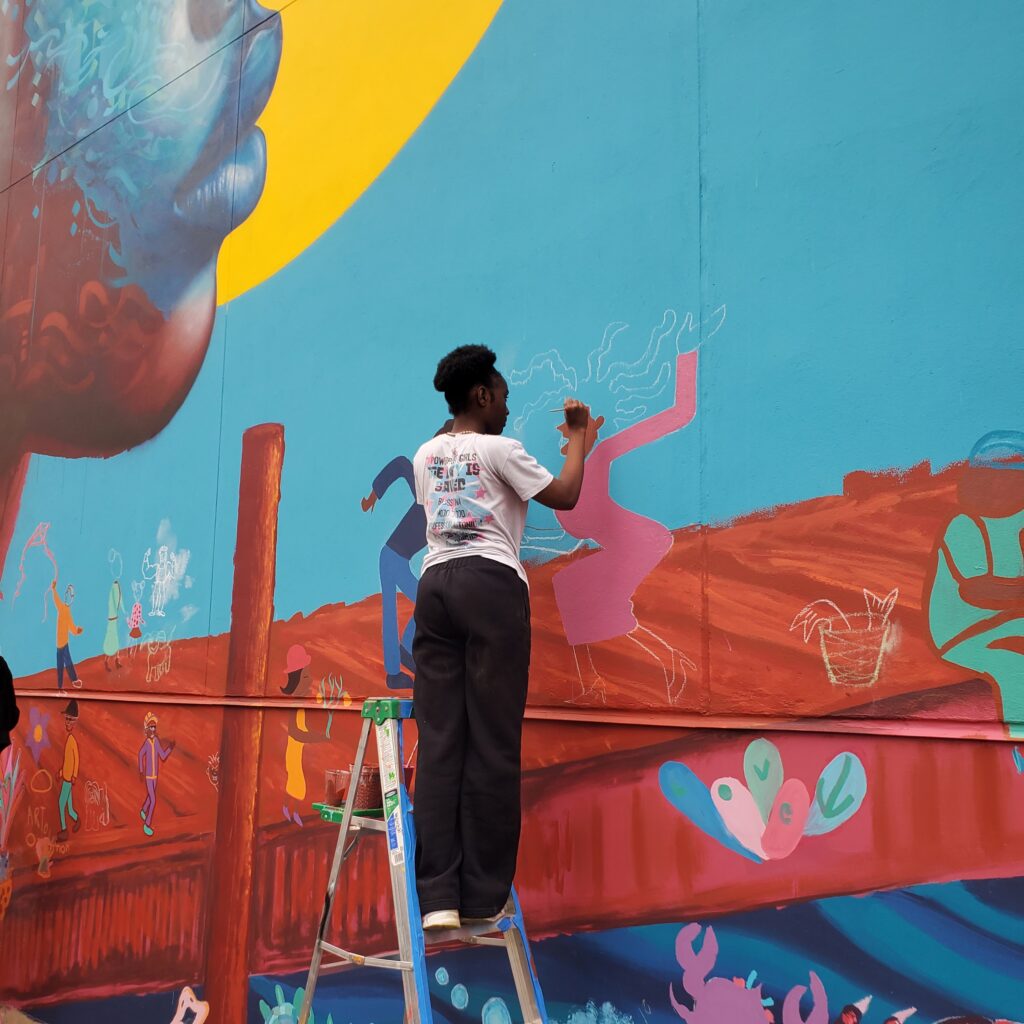 teenage girl standing on ladder painting mural