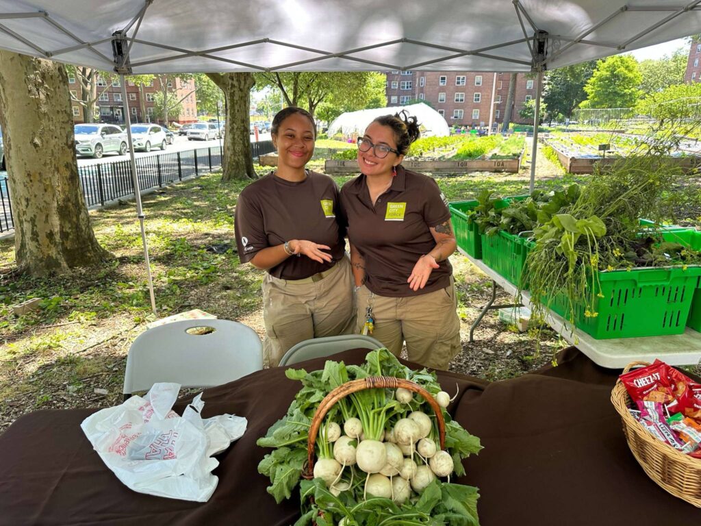 two Green City Force Corps Members standing behind fresh vegetables