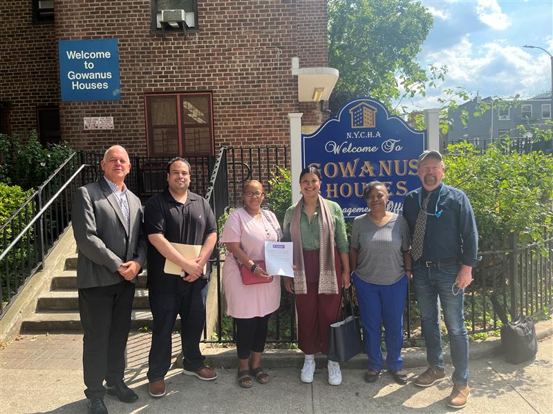 six people standing in front of a building and the Gowanus Houses sign