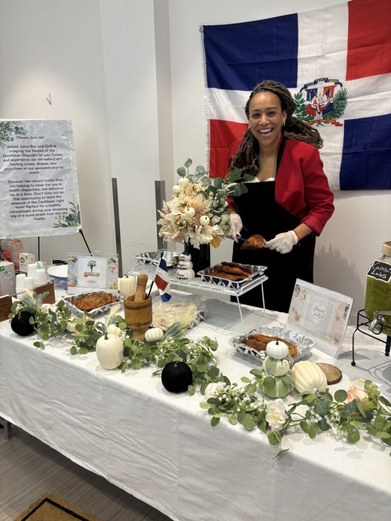 woman standing behind table of food. Dominican Republic flag in the background