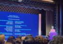 woman on stage at podium next to a large screen with text that says New York City Housing Authority and the projects that won awards along with names of companies/organizations