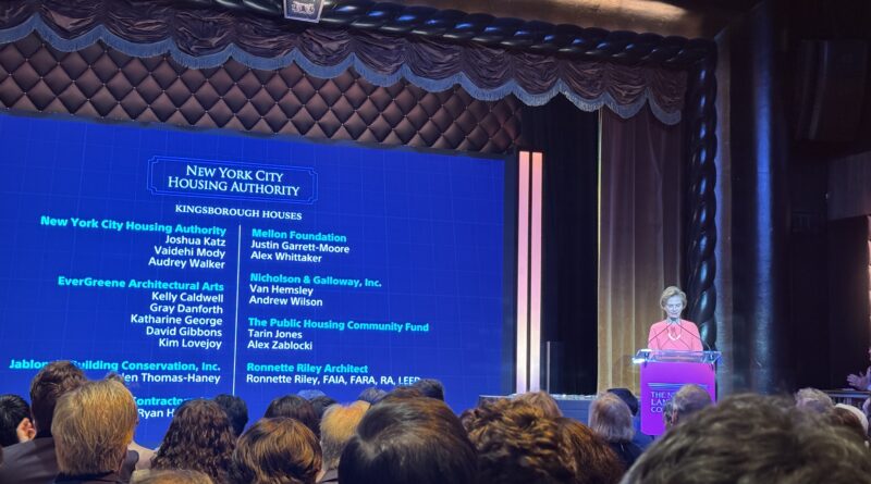 woman on stage at podium next to a large screen with text that says New York City Housing Authority and the projects that won awards along with names of companies/organizations