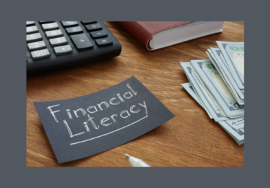 photo of a paper with text that reads, "Financial Literacy" with money, a book, and a calculator on a table.
