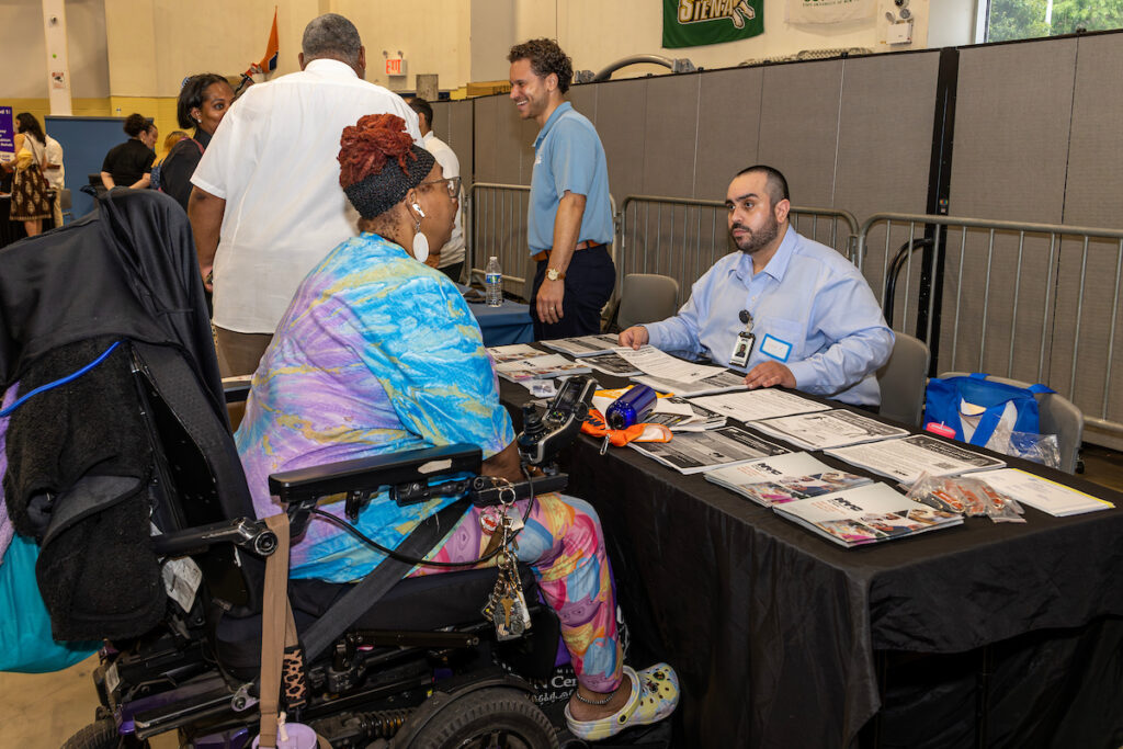 woman in wheelchair talking to man seated behind a table