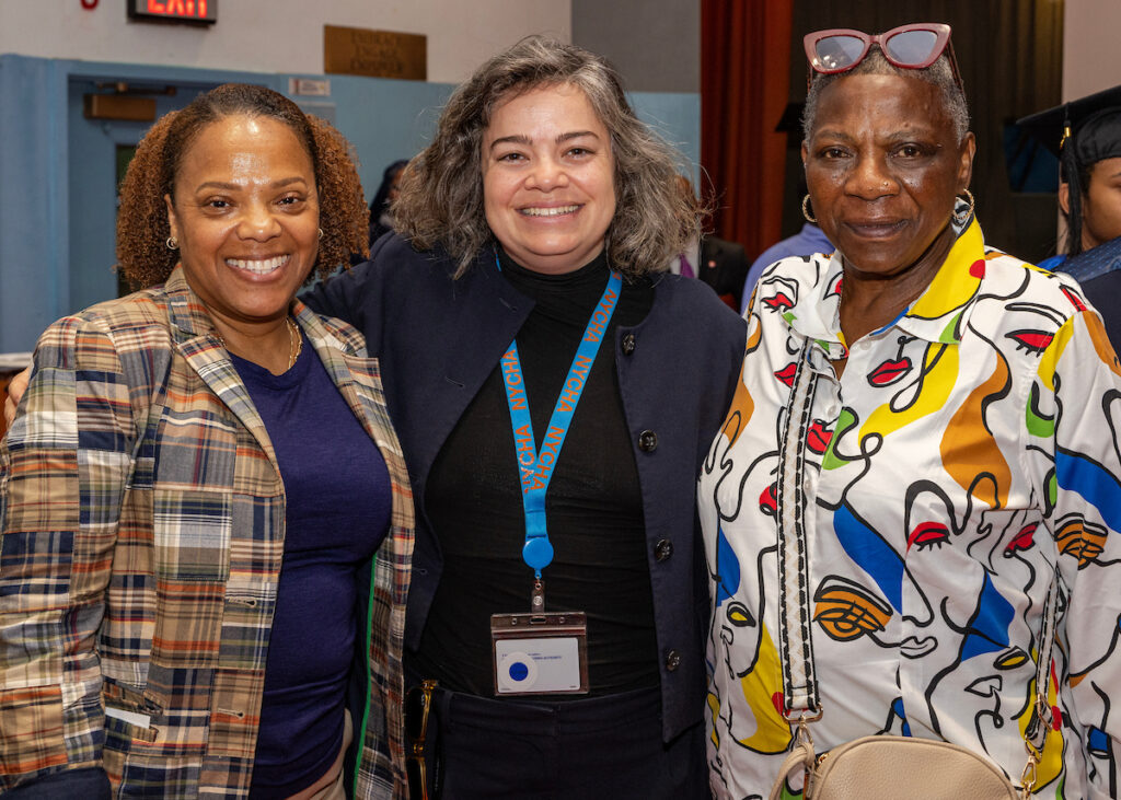 Three individuals pose together at an event, smiling for the camera with one wearing a lanyard and another in a colorful patterned shirt.
