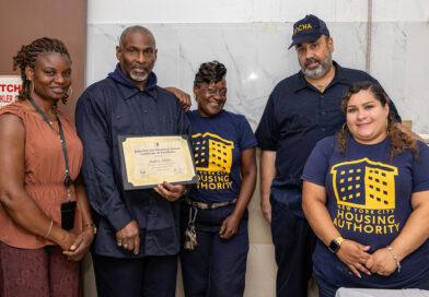 A group of five individuals, including one holding a certificate, stand together in a room with a “New York City Housing Authority” logo on their shirts.