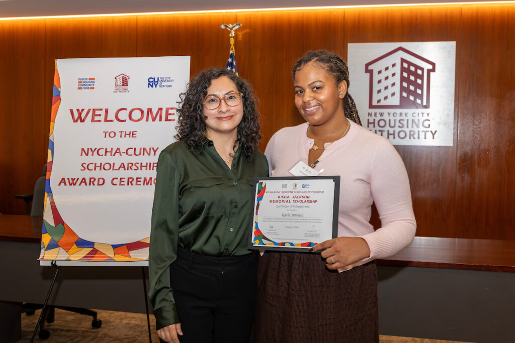 Two individuals stand together at an awards ceremony, one holding a framed certificate recognizing achievement in the NYCHA-CUNY Scholarship Program.