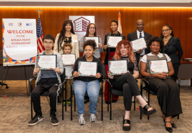 A group of individuals, including youth and adults, pose together at a scholarship award ceremony, holding certificates and standing in front of a welcome banner.