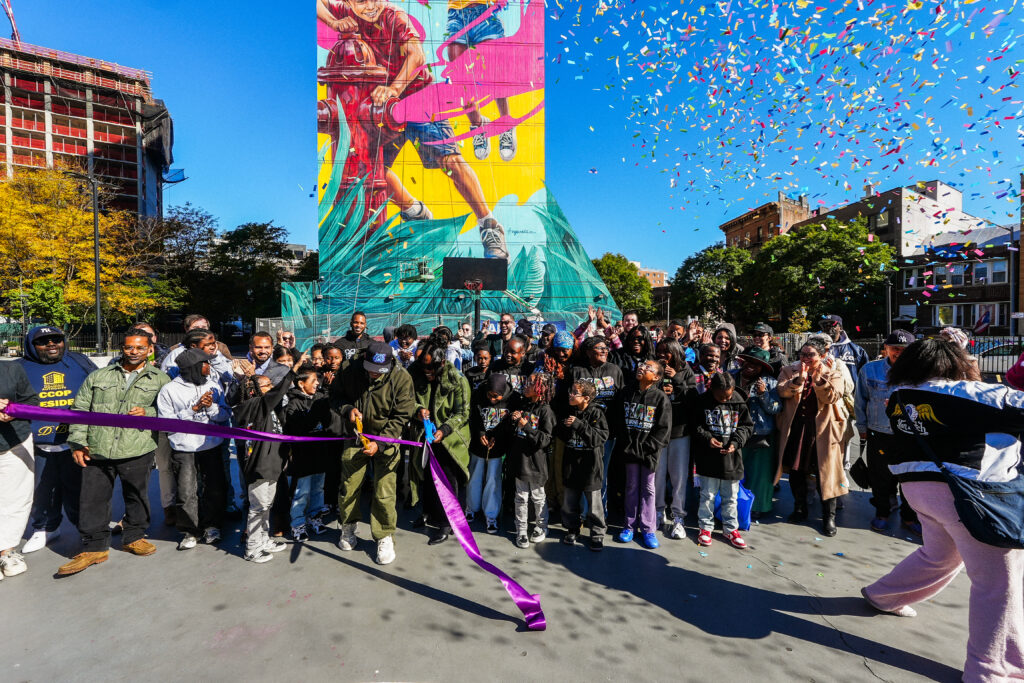 group of people cutting a ribbon in front of a colorful mural, confetti blows in the air
