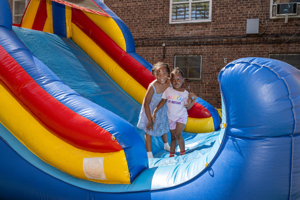 Two children stand on a colorful inflatable slide, smiling for the camera.