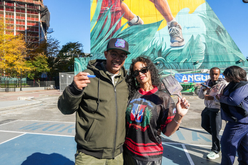 a man and a woman stand in front of a colorful mural