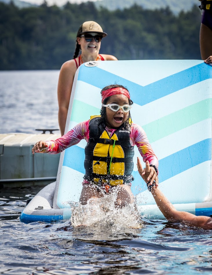 girl in life jacket doing water activities on a lake, while an adult watches on