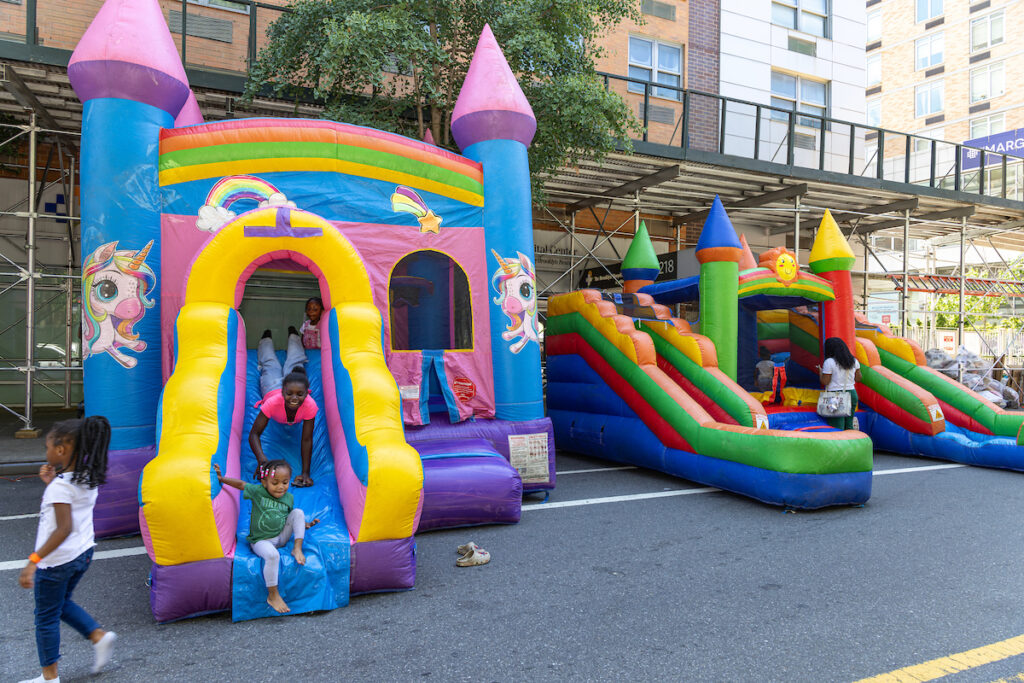 Children play on colorful inflatable bounce houses and slides in an outdoor urban setting.