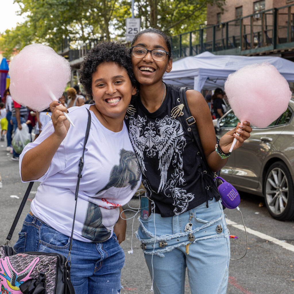 Two people smile while holding pink cotton candy at an outdoor event.