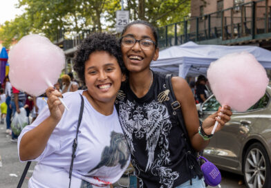 Two people smile while holding pink cotton candy at an outdoor event.