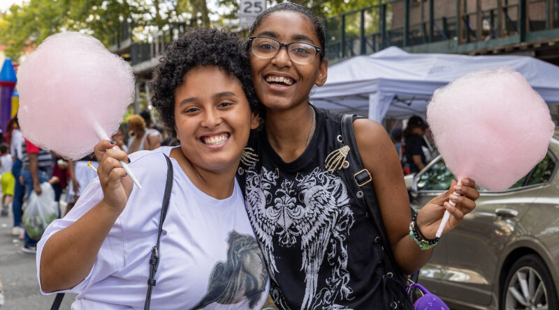 Two people smile while holding pink cotton candy at an outdoor event.