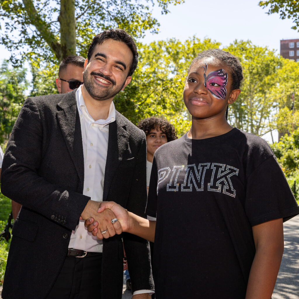 A person in a suit shakes hands with a young individual wearing a butterfly face painting and a black t-shirt.