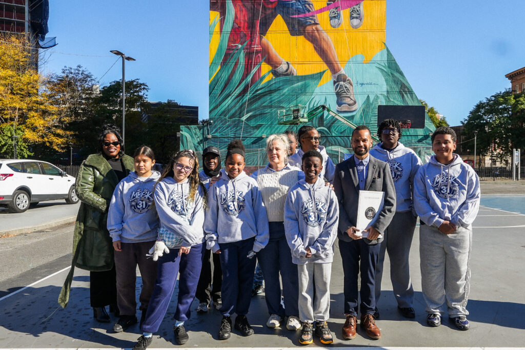 group of tween and teen children pose with a few adults in front of colorful mural