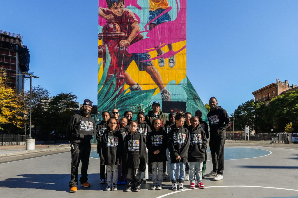 group of children and three adults, all wearing black hoodies, stand in front of colorful mural