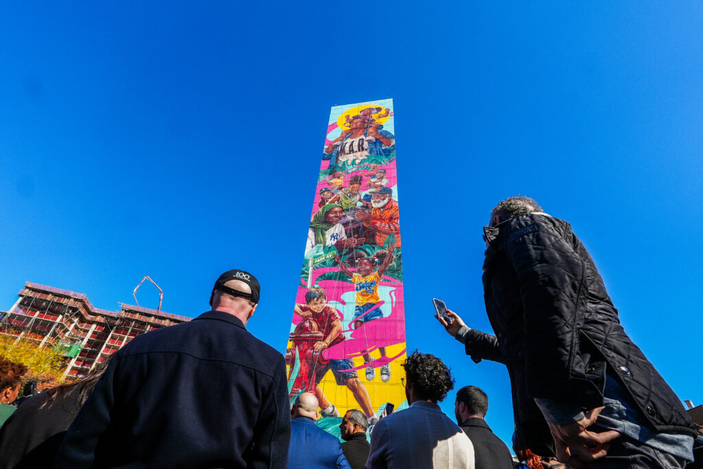 people looking up at a very tall and colorful mural on the side of a building