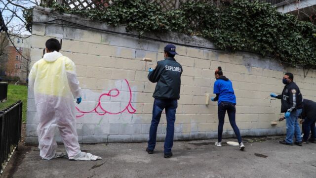 group of people painting over brick wall