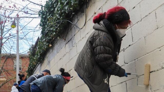 group of people painting over brick wall