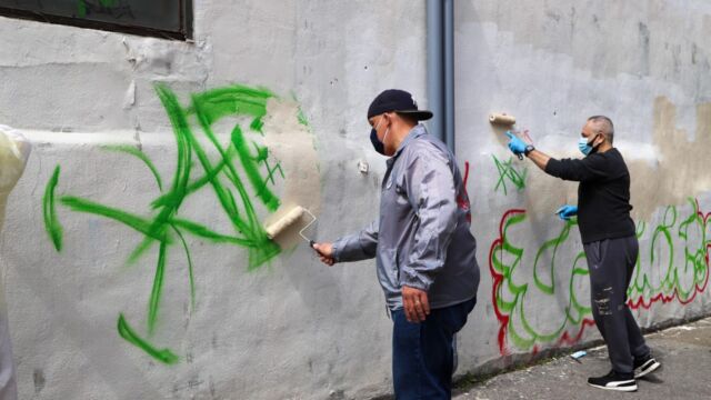 two men painting over graffiti on a wall
