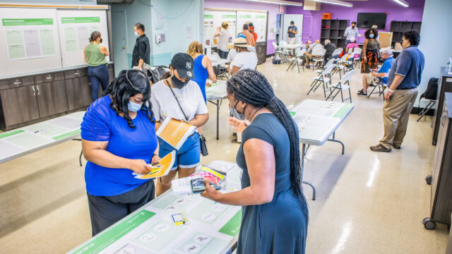 three people standing at a table in a semi-crowded room
