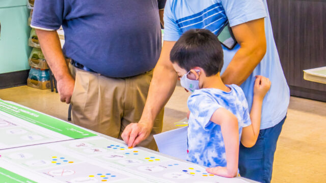 two men and a young boy point to pictures on a table
