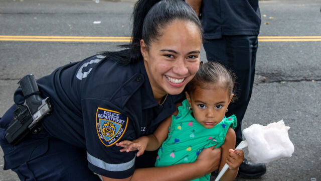 National Night Out Monroe Houses woman police officer and young child holding cotton candy